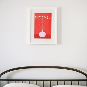 May include: A framed print of a white flower arrangement in a pink vase on a red background with a checkered pattern.