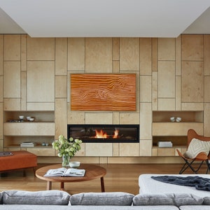 May include: A modern living room with a fireplace and a large TV screen. The walls are made of wood panels and the floor is made of hardwood. There is a couch, a coffee table, and a chair in the room.