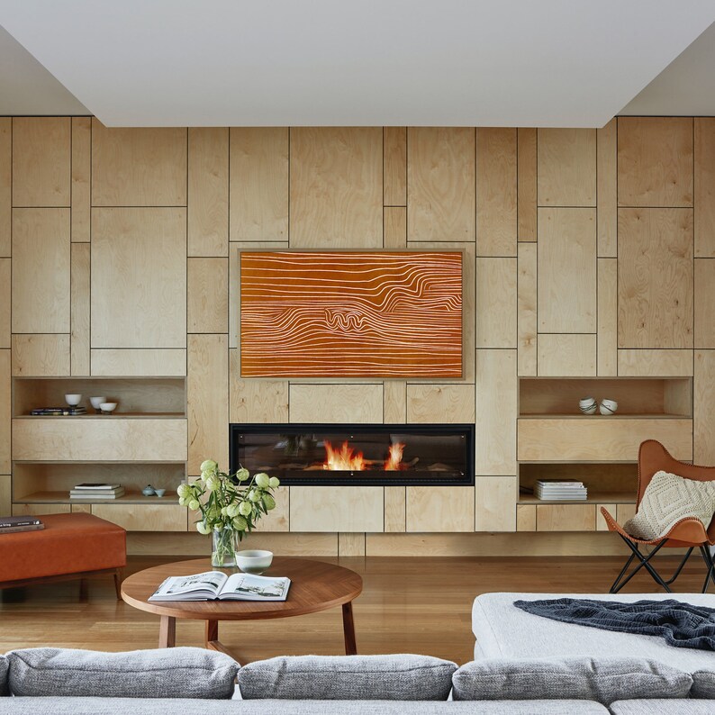 May include: A modern living room with a fireplace and a large TV screen. The walls are made of wood panels and the floor is made of hardwood. There is a couch, a coffee table, and a chair in the room.