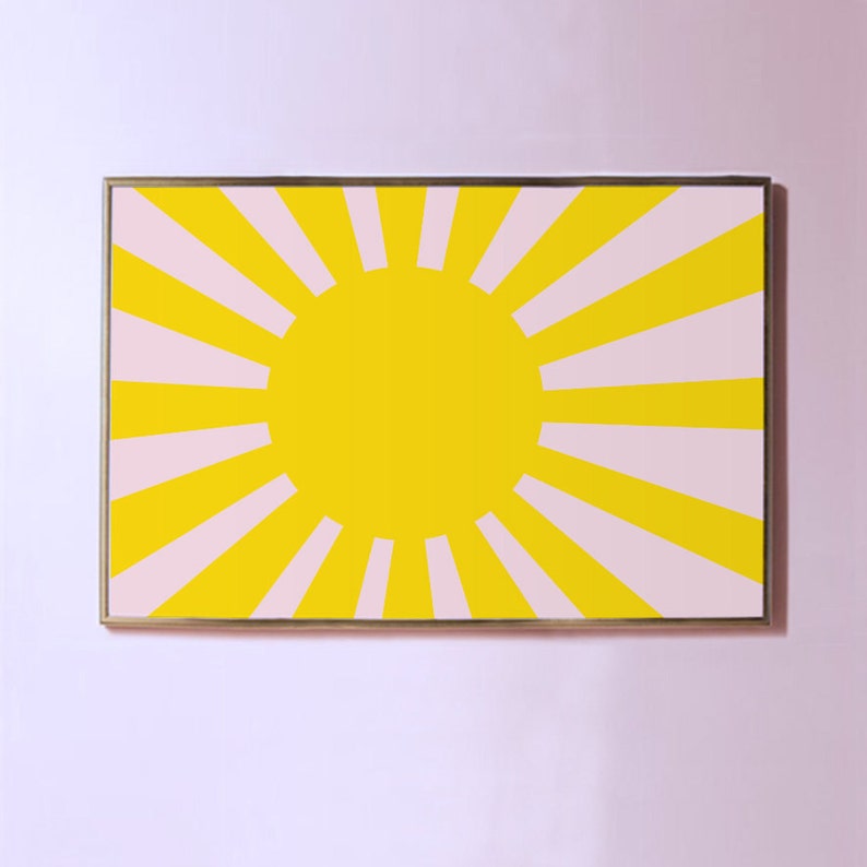 Op de afbeelding: Een ingelijst print met een geel zonnestralenontwerp op een roze achtergrond. De zonnestralen heeft een grote gele cirkel in het midden.