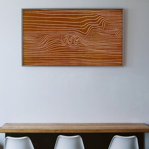 May include: A framed abstract art print with white lines on a brown background. The lines create a wavy pattern.