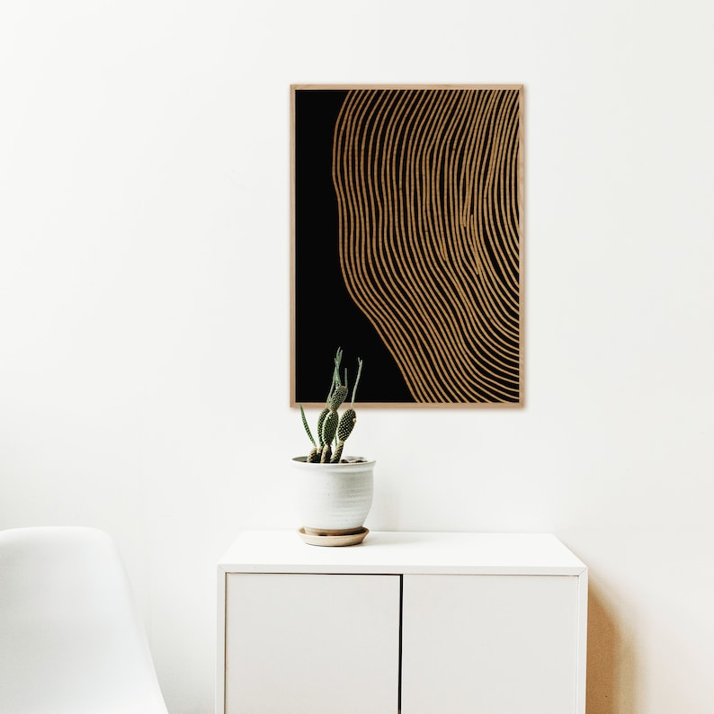 Puede incluir: Impresi&oacute;n de arte abstracto con l&iacute;neas doradas sobre fondo negro. La impresi&oacute;n est&aacute; enmarcada y colgada en una pared blanca.