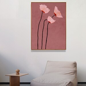 May include: A framed abstract floral art print. The artwork features three pink flowers with black stems against a dusty rose background. The flowers have a textured appearance, and the frame is a light brown color.