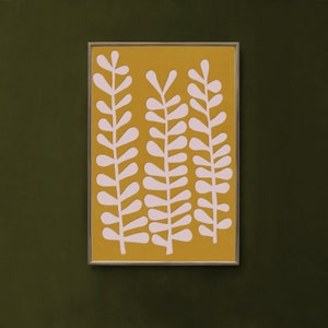 Op de afbeelding: Een ingelijst print met een minimalistisch ontwerp met drie gestileerde roze plantenstengels op een gele achtergrond.