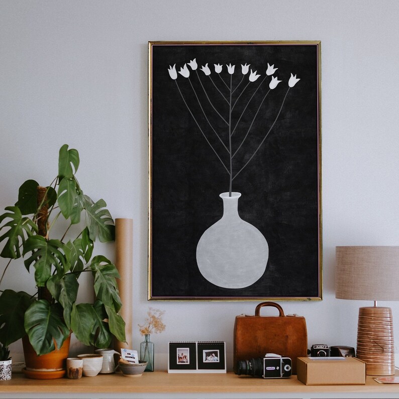 May include: A black and white framed print of a white vase with a white flower stem and white flowers on a black background.