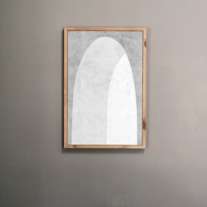 Peut inclure: Une impression d'art abstrait encadr&eacute;e avec un motif blanc et gris de deux arches qui se chevauchent. L'impression est dans un cadre en bois clair.
