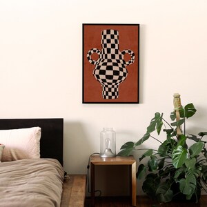 May include: A black and white chequered vase with two handles, on a terracotta background, framed in black.