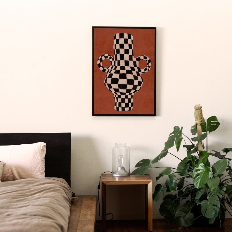 May include: A black and white chequered vase with two handles, on a terracotta background, framed in black.
