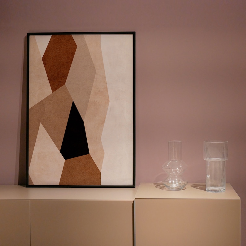 May include: A framed abstract art print with geometric shapes in shades of brown, white, and black. The print is hanging on a light pink wall above a pair of clear glass vases.
