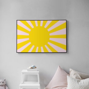 Op de afbeelding: Een ingelijste print van een gele zon met roze stralen die naar buiten stralen. De zon is gecentreerd in de afbeelding en de stralen strekken zich uit tot aan de randen van de lijst.