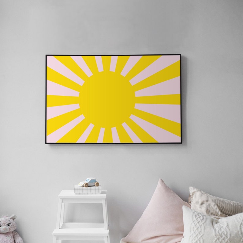 Op de afbeelding: Een ingelijste print van een gele zon met roze stralen die naar buiten stralen. De zon is gecentreerd in de afbeelding en de stralen strekken zich uit tot aan de randen van de lijst.
