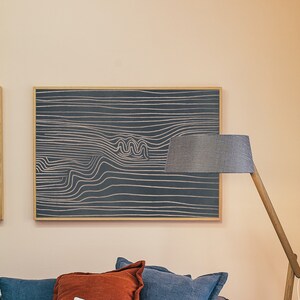 May include: A framed abstract art print with a black background and white lines creating a wavy pattern. The print is hanging on a light peach wall.
