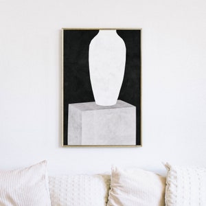 May include: A white vase sits on a gray cube against a black background. The vase is tall and slender with a rounded base and a wide opening at the top. The cube is square and has a textured surface. The background is a solid black.