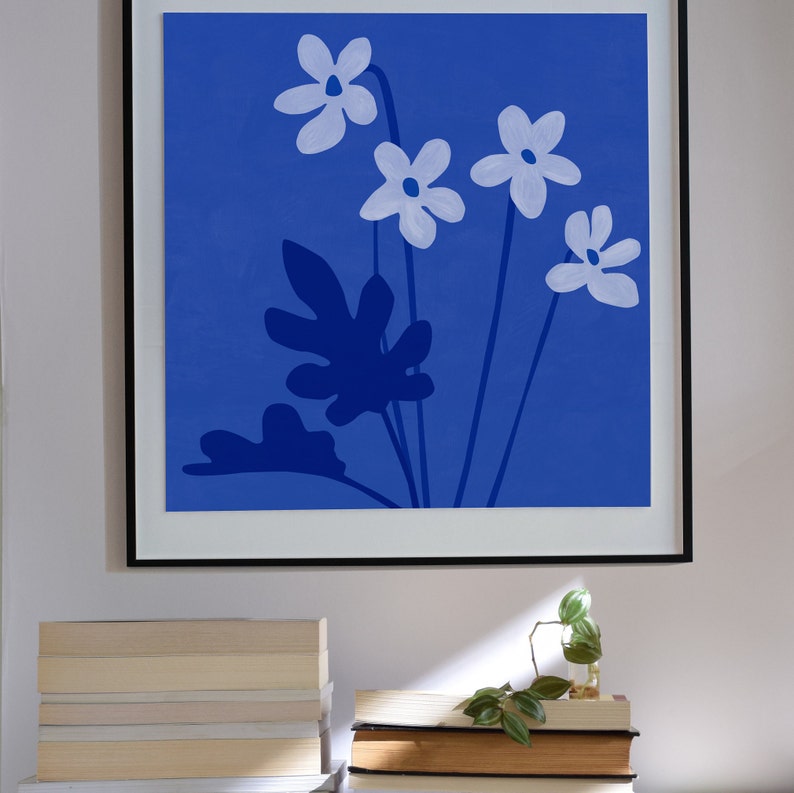Pu&ograve; includere: Una stampa incorniciata di uno sfondo blu con fiori bianchi e foglie blu scuro. I fiori sono stilizzati e hanno cinque petali ciascuno.