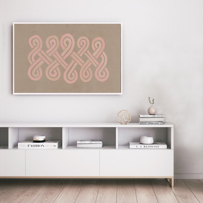 K&ouml;nnte beinhalten: Ein gerahmter Druck eines geometrischen Designs mit rosa und braunen Linien auf beigefarbenem Hintergrund. Der Druck h&auml;ngt an einer wei&szlig;en Wand &uuml;ber einem wei&szlig;en Regal mit B&uuml;chern und Dekorationsgegenst&auml;nden.