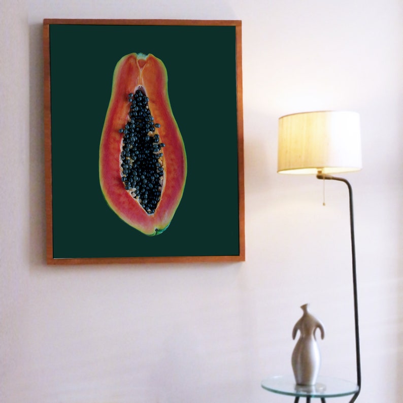 May include: A framed print of a papaya cut in half, showing the black seeds inside. The papaya is on a dark green background.