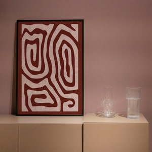 May include: A framed abstract print with a white background and red lines forming a pattern. The print is on a shelf with two clear glass vases.