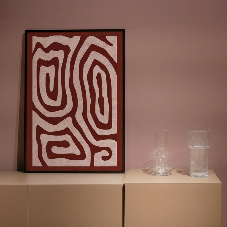 May include: A framed abstract print with a white background and red lines forming a pattern. The print is on a shelf with two clear glass vases.