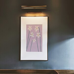 May include: A framed print of a minimalist floral design featuring five white flowers with yellow centers on a light purple background.