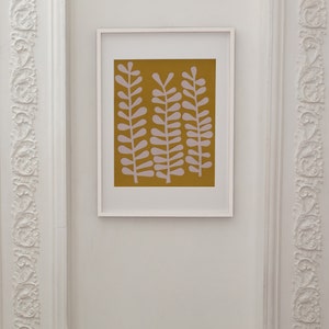 Op de afbeelding: Een ingelijste print met een minimalistisch ontwerp met drie gestileerde roze planten op een mosterdgele achtergrond.