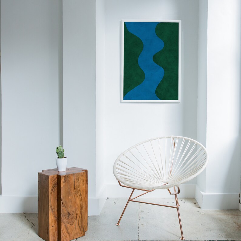 May include: A white chair with a copper frame sits in a room with a white wall and a framed abstract print of a blue and green design.