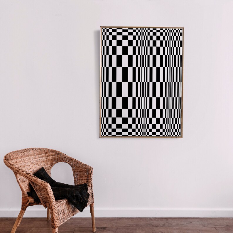 May include: A black and white checkered pattern artwork in a gold frame hanging on a white wall. A wicker chair with a black throw blanket is in the foreground.