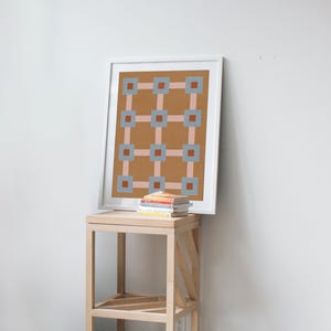 K&ouml;nnte beinhalten: Ein gerahmter Kunstdruck mit einem geometrischen Muster in einem wei&szlig;en Rahmen. Das Kunstwerk zeigt ein Raster aus Quadraten und Linien in Braun-, Rosa- und Blaut&ouml;nen. Der Druck liegt auf einem Beistelltisch aus hellem Holz, darunter ein Stapel B&uuml;cher.