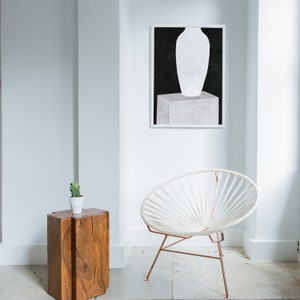 May include: A white vase sits on a white pedestal against a black background. The vase is in a minimalist style and is a simple, modern design. The image is framed in a white frame.