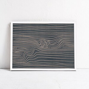 May include: Abstract art print with a white frame. The print features a dark blue background with a pattern of thin, wavy, light brown lines.