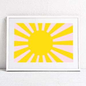 Op de afbeelding: Een ingelijst print met een geel zonnestralenontwerp. De zonnestralen heeft roze stralen die uit een grote gele cirkel in het midden stralen.