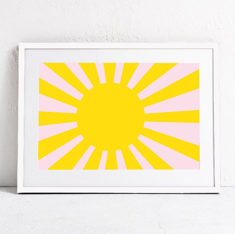 Op de afbeelding: Een ingelijst print met een geel zonnestralenontwerp. De zonnestralen heeft roze stralen die uit een grote gele cirkel in het midden stralen.