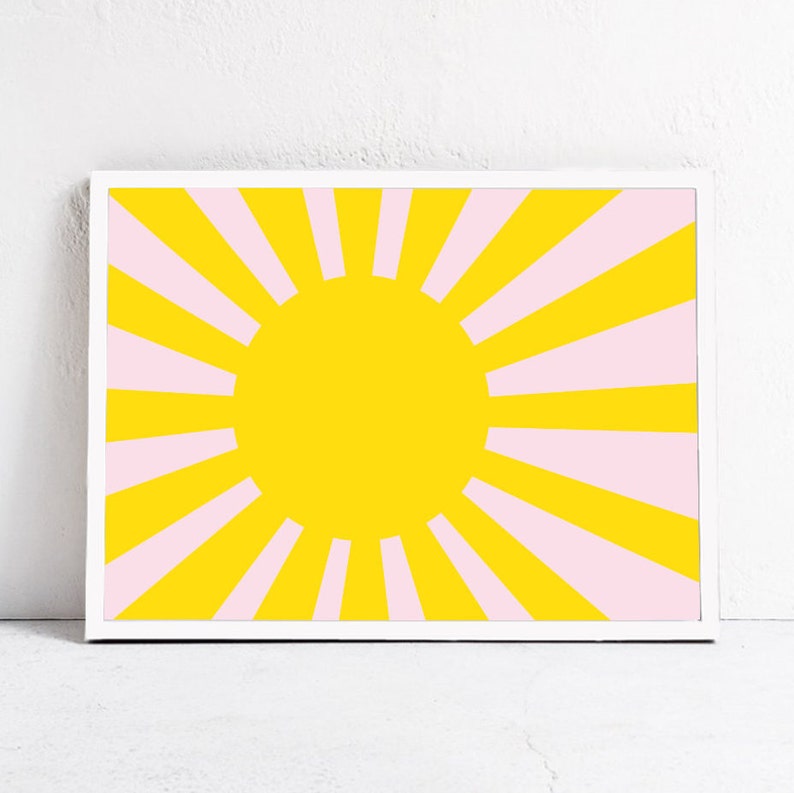 Op de afbeelding: Een ingelijst print met een geel zonnestralenontwerp. De zonnestralen heeft roze stralen die uit een gele cirkel in het midden stralen.