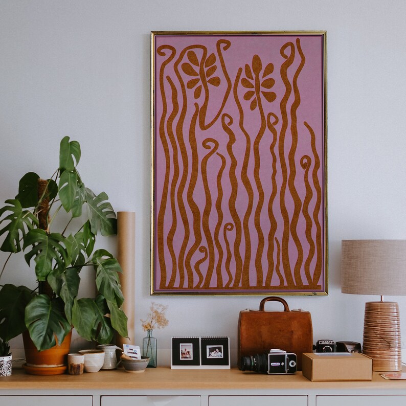 Op de afbeelding: Een ingelijst abstract kunstprint met een roze achtergrond en bruine golvende lijnen die een bloemenpatroon vormen.