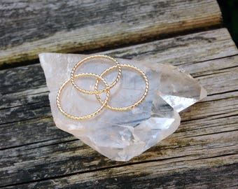 Puede incluir: Tres anillos de metal retorcidos de color dorado apilados uno encima del otro sobre un cristal de cuarzo transparente.