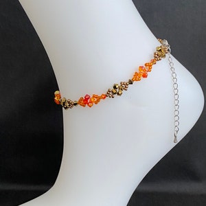 Op de afbeelding: Een oranje, gouden en bruine kralen enkelband met een zilveren kettingverlenger.