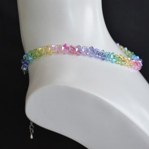 May include: A rainbow crystal necklace with a silver clasp. The necklace is made of small, faceted crystals in shades of green, yellow, orange, pink, purple, and blue.