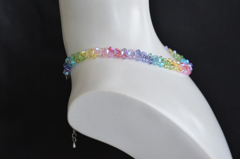 May include: A rainbow crystal necklace with a silver clasp. The necklace is made of small, faceted crystals in shades of green, yellow, orange, pink, purple, and blue.