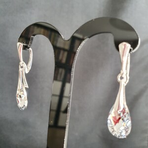 May include: A pair of silver teardrop earrings with clear crystal stones hanging from a silver hook.