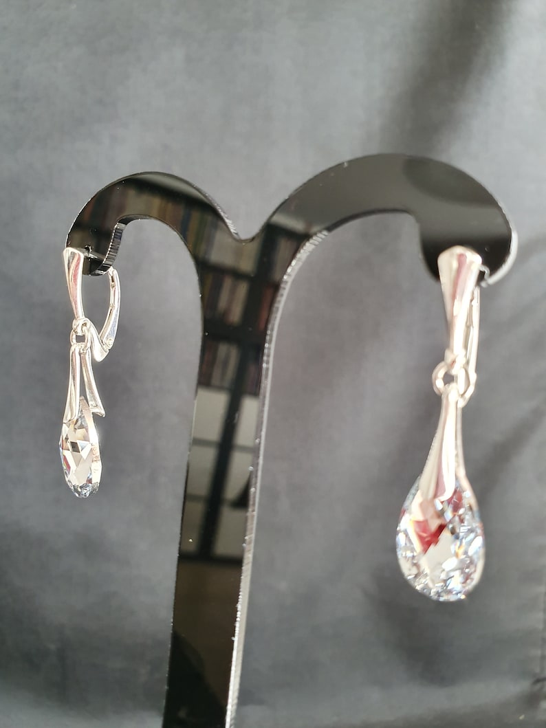 May include: A pair of silver teardrop earrings with clear crystal stones hanging from a silver hook.