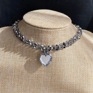 May include: A silver choker necklace with a large crystal heart pendant. The necklace is made of small, faceted beads and is layered for a dramatic look.