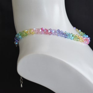 May include: A rainbow crystal choker necklace with a silver clasp. The necklace is made of small, faceted crystals in shades of green, yellow, pink, blue, and purple.