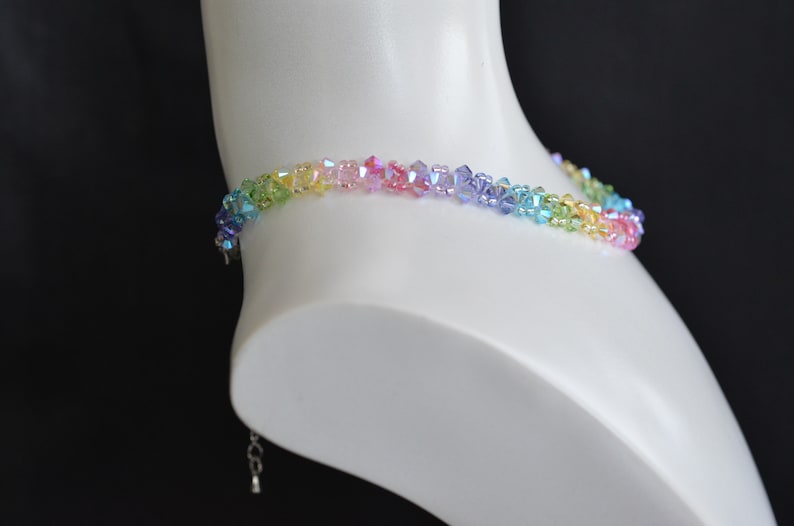 May include: A rainbow crystal choker necklace with a silver clasp. The necklace is made of small, faceted crystals in shades of green, yellow, pink, blue, and purple.