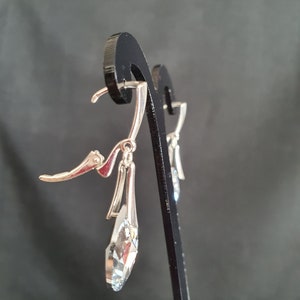 May include: Silver dangle earrings with a clear crystal teardrop pendant. The earrings have a lever back closure.