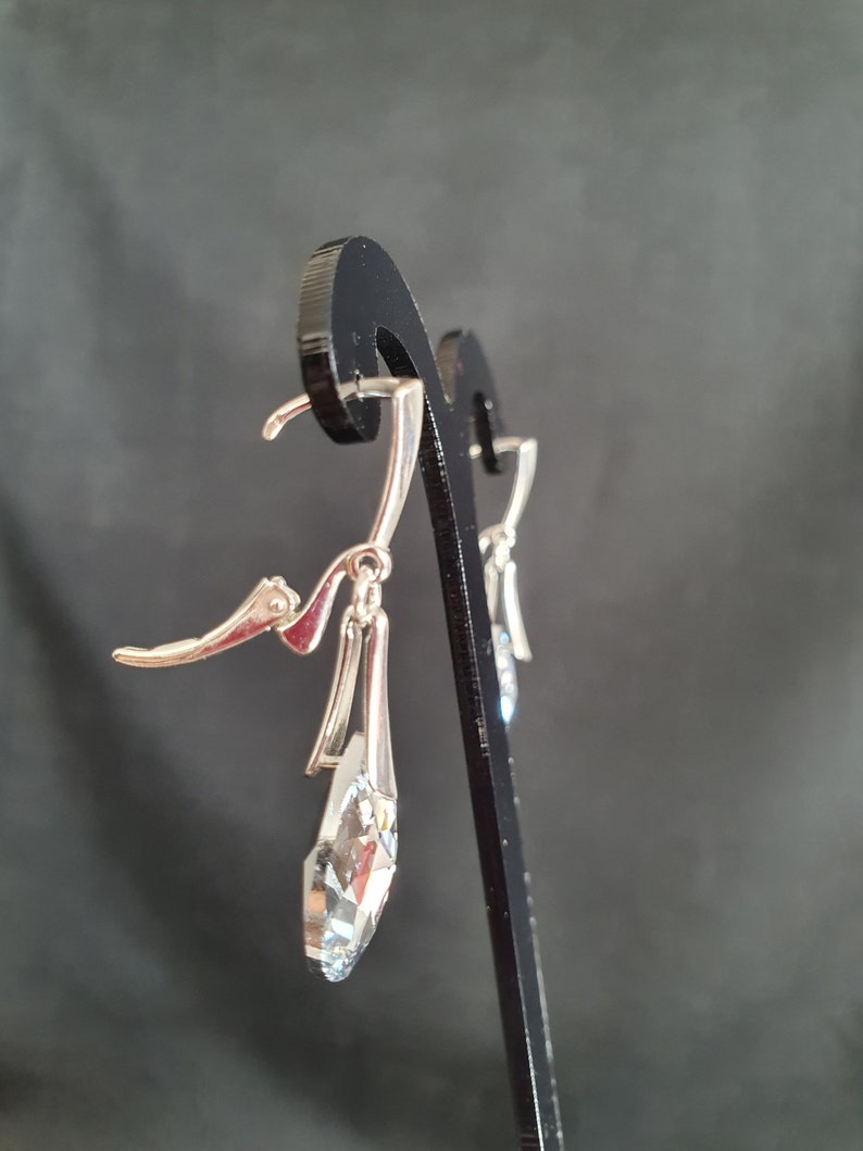 May include: Silver dangle earrings with a clear crystal teardrop pendant. The earrings have a lever back closure.