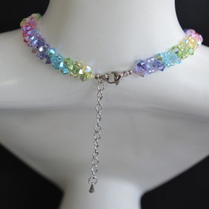 May include: A rainbow crystal necklace with a silver clasp and chain. The necklace is made of small, faceted crystals in shades of pink, orange, yellow, green, blue, and purple.