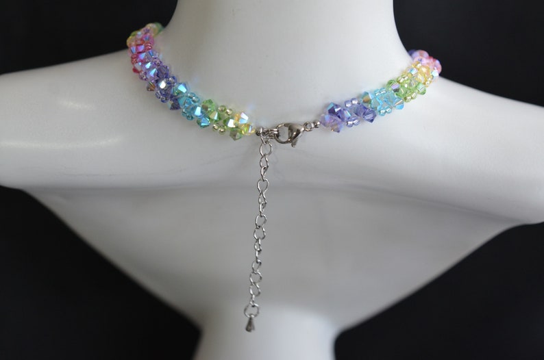 May include: A rainbow crystal necklace with a silver clasp and chain. The necklace is made of small, faceted crystals in shades of pink, orange, yellow, green, blue, and purple.