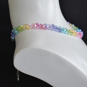 May include: A rainbow crystal choker necklace with a silver clasp. The necklace is made of small, faceted crystals in shades of green, yellow, orange, pink, purple, and blue.