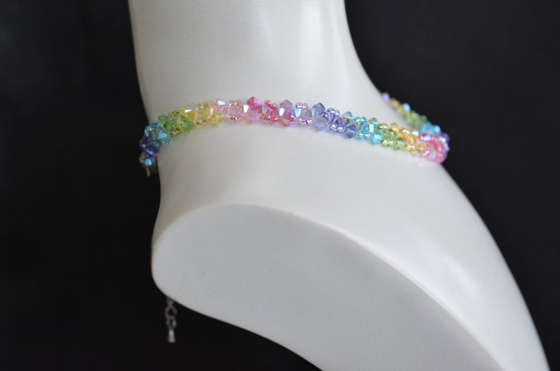 May include: A rainbow crystal choker necklace with a silver clasp. The necklace is made of small, faceted crystals in shades of green, yellow, orange, pink, purple, and blue.