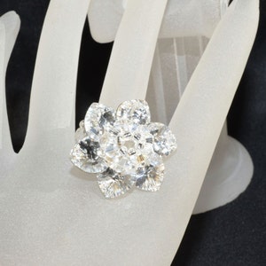 May include: A silver ring with a large, clear crystal flower design.