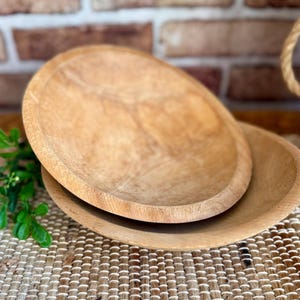 May include: Two round, light brown wooden bowls with visible natural grain patterns. The bowls are stacked, with the smaller bowl resting inside the larger one, showcasing a smooth, unfinished texture and a simple, circular design.